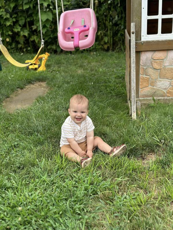 A baby sitting on the grass by the swing set