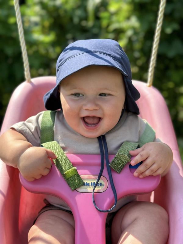 A laughing baby in a sun hat on the swing