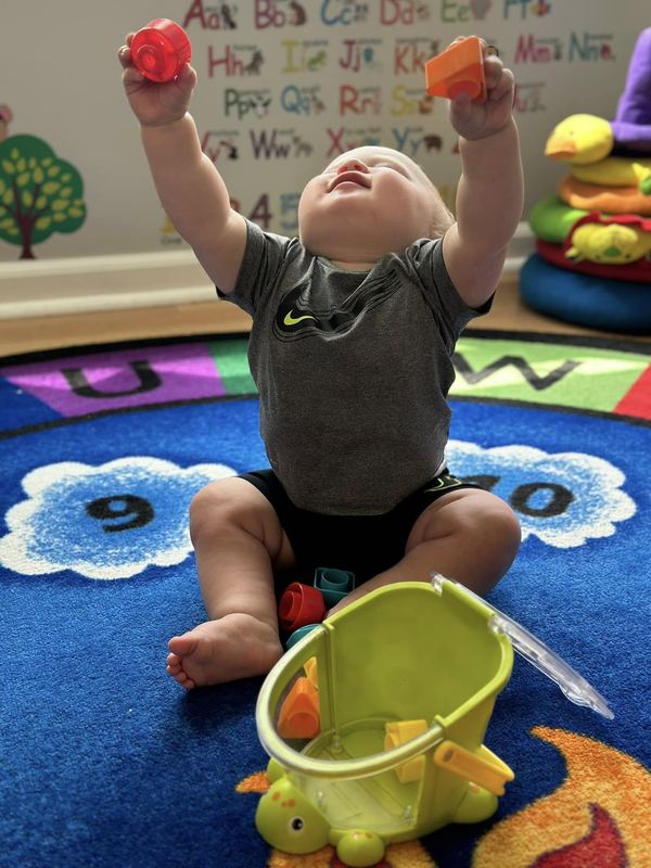 A baby holding toys up high on the rug