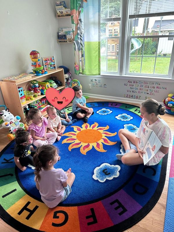 A teacher reading a book to children on the sunshine rug