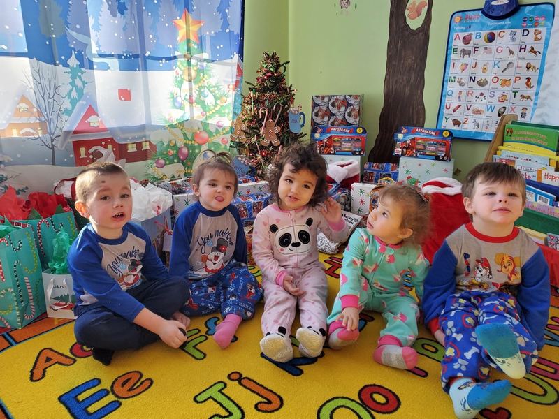 Five toddlers in holiday pajamas lined up on the rug