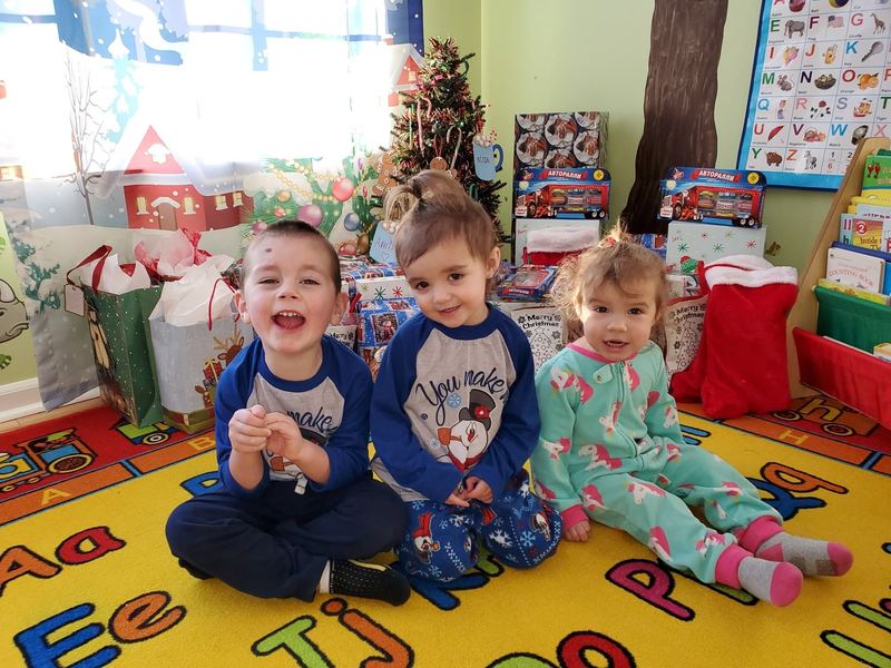 Three toddlers smiling in front of wrapped presents