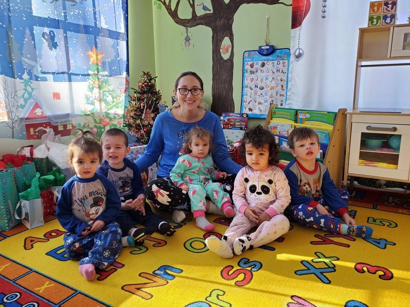 A teacher sitting with children in holiday pajamas