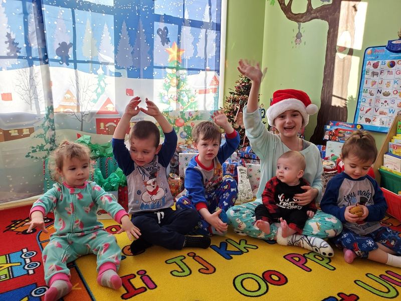Children in holiday pajamas waving on the alphabet rug