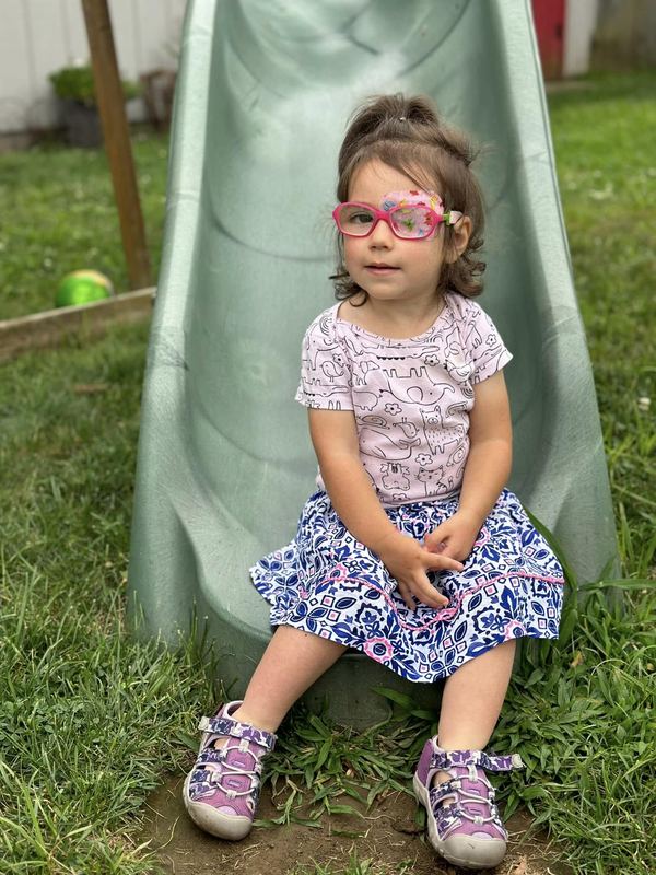 A little girl in pink glasses sitting at the bottom of the slide