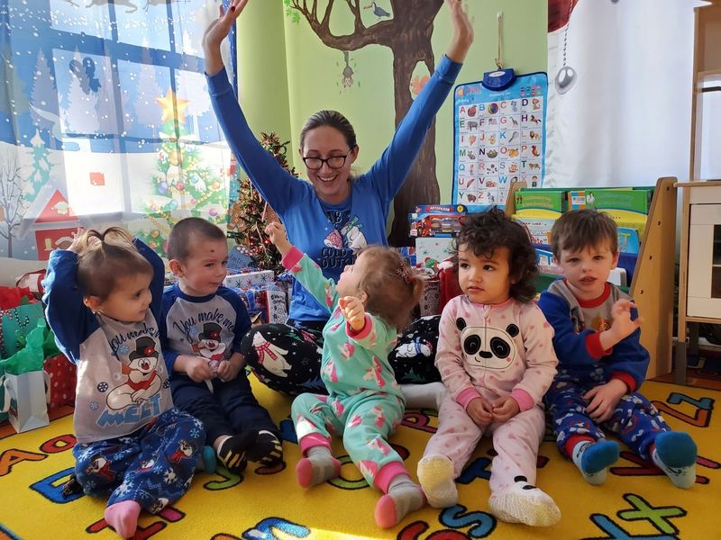 A teacher cheering with arms up behind a row of toddlers