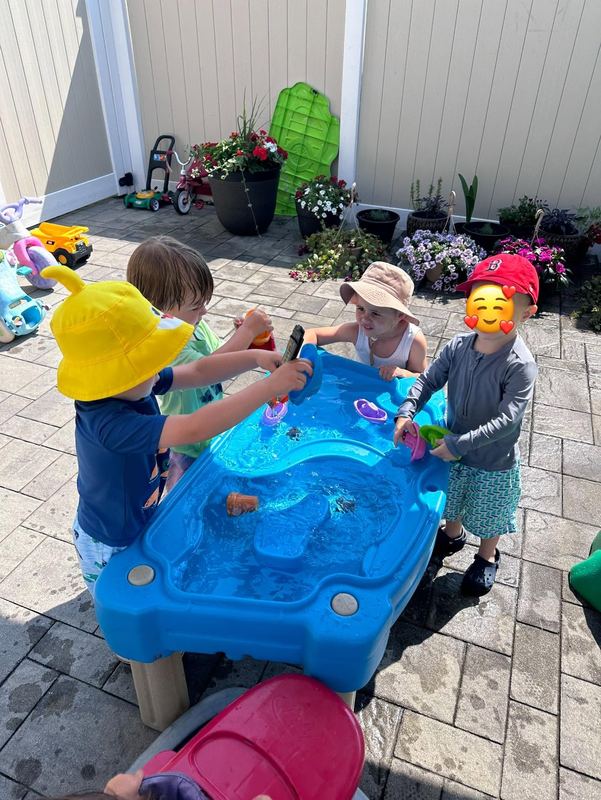 Children in sun hats playing at the water table on the patio